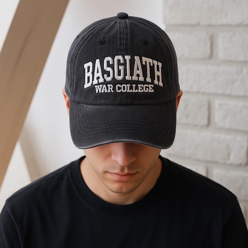 May include: Black baseball cap with the text "BASGIATH WAR COLLEGE" in white, distressed lettering. The cap has a curved brim and a small, black button on top. The cap is worn by a person wearing a black shirt.