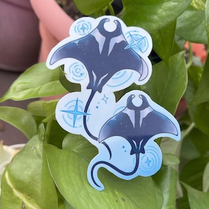 May include: Two blue and black manta ray stickers with white outlines and sparkling stars on a green plant.