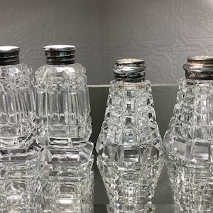Könnte beinhalten: Vier klare Glassalz- und Pfefferstreuer mit silbernen Oberteilen. Die Streuer haben ein strukturiertes, facettiertes Design.