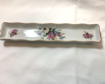 May include: A rectangular, white porcelain dish with a scalloped edge and gold trim. The dish is decorated with floral arrangements in pink, blue, and yellow. The dish measures approximately 10 inches long.