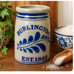 Puede incluir: Una vasija de gres cil&iacute;ndrica con acabado beige moteado, que presenta motivos de hojas pintados a mano en azul y el texto azul BURLINGTON EST. 1865. El recipiente tiene un borde grueso y redondeado y un cuerpo de lados rectos.