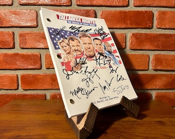 May include: A script from the movie "Talladega Nights: The Ballad of Ricky Bobby" with signatures, displayed on a wooden stand. The script cover features the movie title, cast photos, and an American flag design.