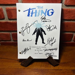 May include: A white sheet of paper with the title "THE THING" in blue, with signatures and a silhouette of a figure with a burst of light. The screenplay is based on "Who Goes There?" by John W. Campbell.
