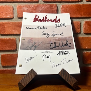 May include: A white script with the title "Badlands" in maroon script, featuring multiple signatures. The script is propped up on a wooden stand against a brick wall.