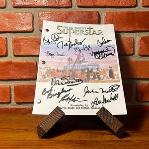 May include: A script page for "Jesus Christ Superstar" featuring multiple signatures, displayed on a wooden stand. The background is a brick wall. The title is at the top, with the screenplay by Melvyn Bragg and Norman Jewison.
