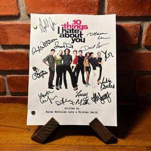 May include: A signed script from the film "10 Things I Hate About You" featuring the title of the film and the names of the actors and writers. The script is white with black text and is signed in black ink.