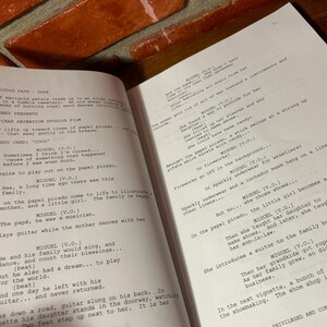 May include: Open book with script pages from a film, likely a Pixar animation. The text includes character names and dialogue, with the title "Coco" visible. The pages are on a wooden surface.