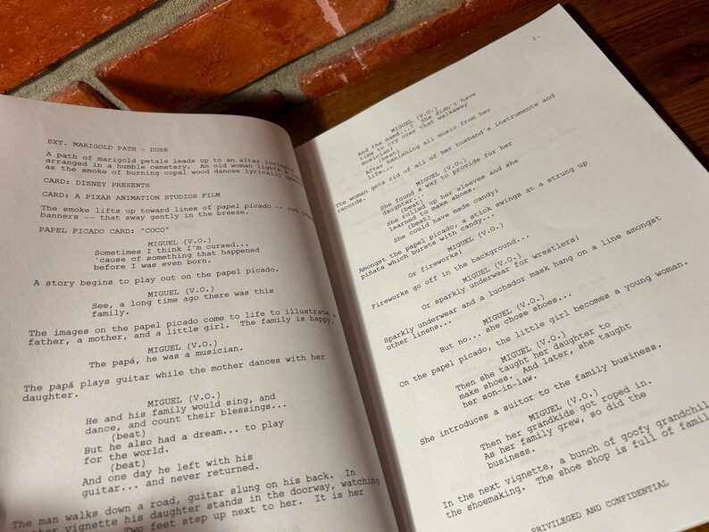 May include: Open book with script pages from a film, likely a Pixar animation. The text includes character names and dialogue, with the title "Coco" visible. The pages are on a wooden surface.