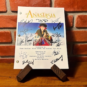 Puede incluir: Un guion de la película de animación "Anastasia" se muestra en un soporte de madera. El guion presenta el título de la película, ilustraciones de personajes y numerosas firmas. El fondo incluye una pared de ladrillo y una superficie de madera.