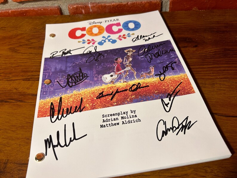 May include: A signed Disney Pixar Coco movie script. The cover features the movie title in colorful letters and an illustration of characters. The script is signed by several people in black ink. The screenplay is by Adrian Molina and Matthew Aldrich.