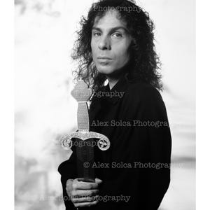 May include: A monochrome portrait of a person holding a decorative sword with an ornate silver handle and a dark blade. The person is wearing a black shirt. The image includes the text "Photography" and "Alex Solca Photography".