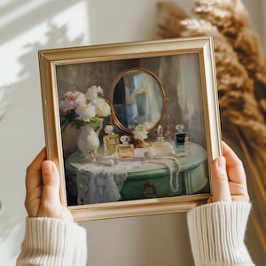 May include: A framed painting depicts a vanity scene with a round mirror, perfume bottles, and a vase of flowers. The vanity is a light green color, and a pearl necklace is draped across the top. The frame is gold.