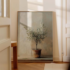 May include: A framed painting of a potted olive tree with green leaves against a light beige background. The tree is in a terracotta pot and is illuminated by a beam of sunlight.
