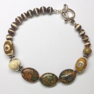May include: A brown and white agate stone bracelet with a silver clasp. The bracelet features a variety of different sized and shaped beads, including some with a brown and white striped pattern.