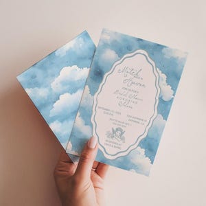 May include: Two light blue and white cloud-themed invitations. One invitation is open, revealing text within a decorative frame. The text reads "Match in Heaven" and details for a bridal shower. The other invitation is folded, showing the cloud design.