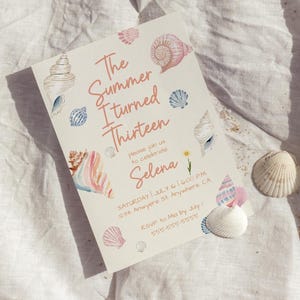 Pu&ograve; includere: Un invito color crema con illustrazioni di conchiglie ad acquerello e il testo "The Summer I turned Thirteen" in corallo. L'invito include i dettagli dell'evento e conchiglie.