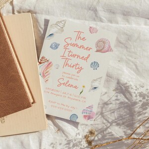 Puede incluir: Una tarjeta de invitaci&oacute;n blanca con el texto "The Summer I turned Thirty" e ilustraciones de conchas marinas. La tarjeta incluye detalles del evento: fecha, hora, lugar e informaci&oacute;n de RSVP. La tarjeta est&aacute; junto a dos libros.
