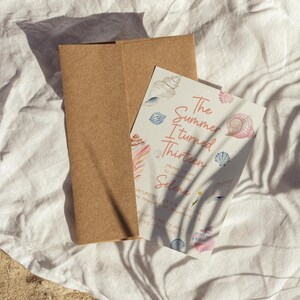 Pu&ograve; includere: Una busta di carta marrone con un biglietto d'invito bianco. Il biglietto riporta il testo "The Summer I Turned Thirteen" con illustrazioni di conchiglie. L'invito &egrave; per il compleanno di Selena.