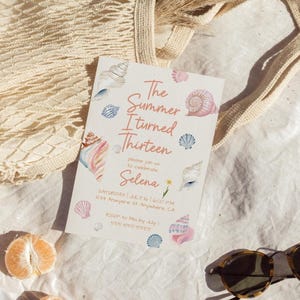 Pu&ograve; includere: Un biglietto d'invito bianco con il testo "The Summer I turned Thirteen" e illustrazioni di conchiglie. Il biglietto include i dettagli dell'evento ed &egrave; circondato da una borsa beige, occhiali da sole e spicchi d'arancia, creando un tema estivo.