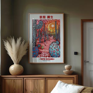 May include: A framed art print featuring a colorful illustration with the text "YAYOI KUSAMA" and Japanese characters. The artwork depicts a surreal landscape with cacti and polka dots. The print is displayed above a wooden cabinet.