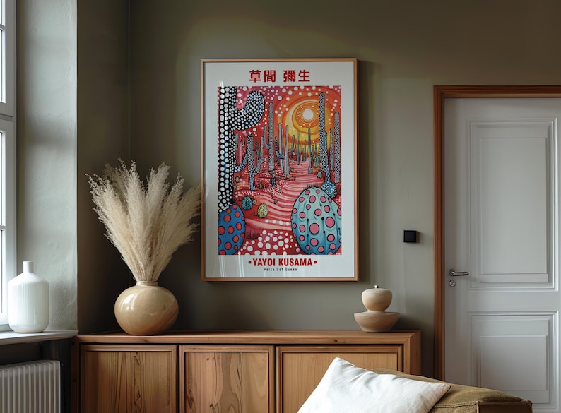 May include: A framed art print featuring a colorful illustration with the text "YAYOI KUSAMA" and Japanese characters. The artwork depicts a surreal landscape with cacti and polka dots. The print is displayed above a wooden cabinet.