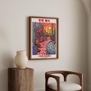 May include: A framed art print featuring a colorful desert landscape with cacti and dotted patterns. The artwork includes Japanese text and the artist's name, Yayoi Kusama, in white lettering. The print is displayed in a room with a wooden chair and a vase.