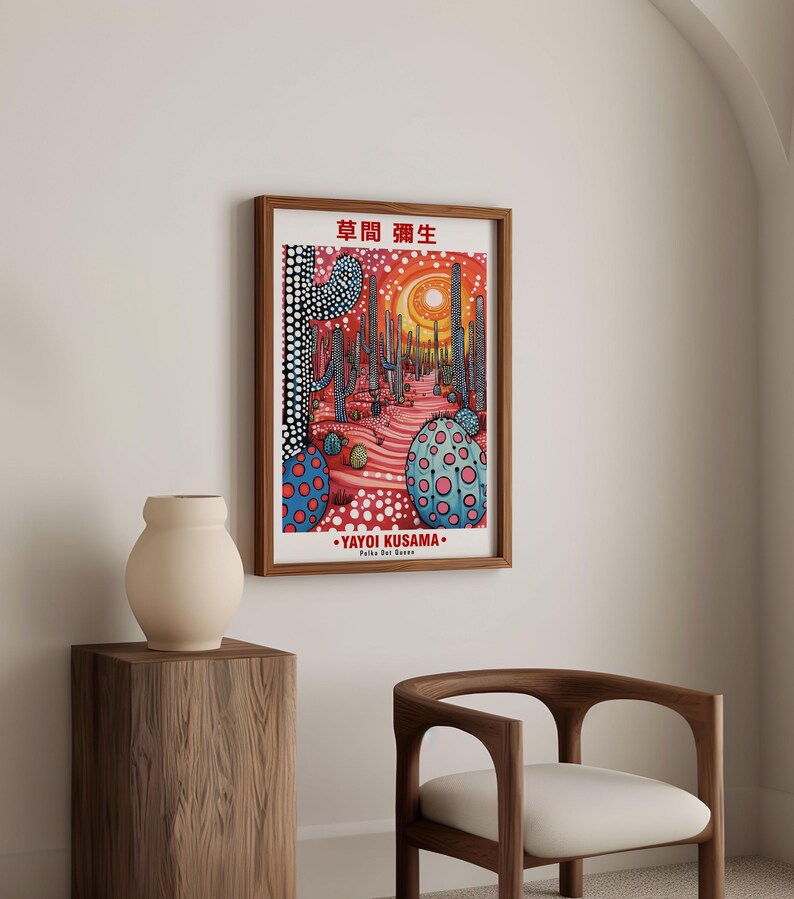 May include: A framed art print featuring a colorful desert landscape with cacti and dotted patterns. The artwork includes Japanese text and the artist's name, Yayoi Kusama, in white lettering. The print is displayed in a room with a wooden chair and a vase.