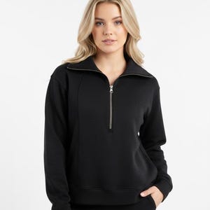 May include: A black sweatshirt with a zip-up collar. The long-sleeved top has a silver zipper and a tailored fit. The model is wearing the sweatshirt with black pants. The background is white.