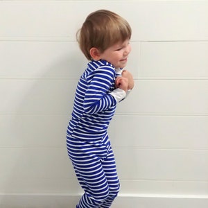 以下が含まれることがあります： 青と白のストライプの長いパジャマを着た小さな子供。子供は白黒の模様のタイル張りの床の上に立っています。