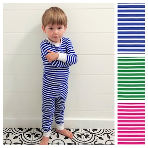 以下が含まれることがあります： 青と白のストライプのパジャマを着た幼い子供。パジャマは長袖のシャツと長いズボンです。