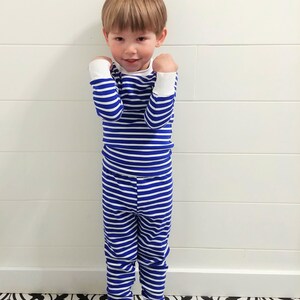 以下が含まれることがあります： 青と白のストライプのパジャマを着た小さな子供。パジャマは長袖の上着と長いズボンです。