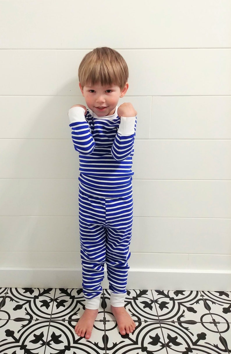 以下が含まれることがあります： 青と白のストライプのパジャマを着た小さな子供。パジャマは長袖の上着と長いズボンです。