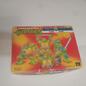 May include: Teenage Mutant Ninja Turtles Heroes in a Half Shell Card Game box art featuring four Teenage Mutant Ninja Turtles characters in green, red, and blue. The box is red, yellow, and white with the text "Teenage Mutant Ninja Turtles" and "Heroes in a Half Shell Card Game".