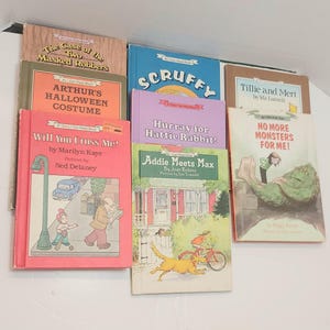 May include: A selection of children's books with vibrant covers. Titles include "The Case of the Two Masked Robbers," "Arthur's Halloween Costume," and "Will You Cross Me?" The books are stacked, displaying various illustrations.
