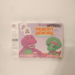 May include: A boxed Barney the Dinosaur Memory Game. The box features Barney and Baby Bop, with the game title in yellow and red. Text on the box includes "Can you remember what's hiding where!" and "Flip the cards to make a pair!"