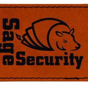 Puede incluir: Un parche de cuero marrón con costuras negras y el texto "Armadillo Security" y una silueta negra de un armadillo.