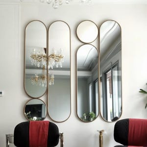 Könnte beinhalten: Ein Wohnzimmer-Interieur mit modernem Design, das einen Kristall-Kronleuchter, drei ovale Spiegel und zwei rot-schwarze Stühle mit goldenen Akzenten zeigt.