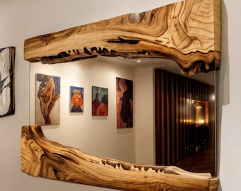 May include: A rectangular mirror with a natural wood frame. The frame is made from a single piece of light brown wood with a unique, organic shape. The mirror reflects a hallway with artwork on the wall.