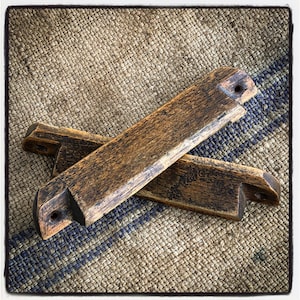 May include: Two rustic wooden drawer pulls with a dark brown finish and a distressed look. The pulls have a simple, rectangular shape with rounded edges and two small holes for mounting.