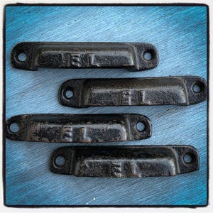 May include: Four black metal drawer pulls with a slightly rounded rectangular shape. Each pull has a small, raised number on the front: 151, 51, 51, and 5.