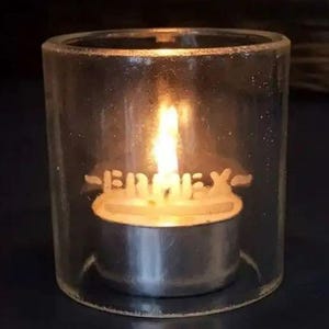 May include: A clear glass candle holder with a tea light inside. The candle holder has the word "Happy" etched into the glass.