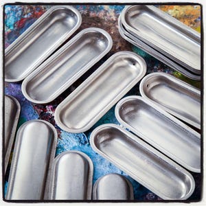 Op de afbeelding: Een verzameling ovale containers van zilverkleurig metaal, mogelijk voor verf of andere kleine voorwerpen, gerangschikt op een kleurrijke achtergrond.