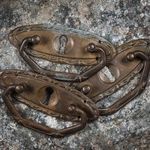 May include: Four antique brass drawer pulls with ornate designs and keyholes. The pulls have a worn, aged patina.