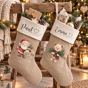 Könnte beinhalten: Zwei Weihnachtsstrümpfe aus Jute mit weißen Bündchen. Der linke Strumpf trägt den Namen Paul und ein Weihnachtsmann-Motiv. Der rechte Strumpf trägt den Namen Emma und ein Teddybären-Motiv. Beide sind mit kleinen Geschenken und Tannenzweigen gefüllt.