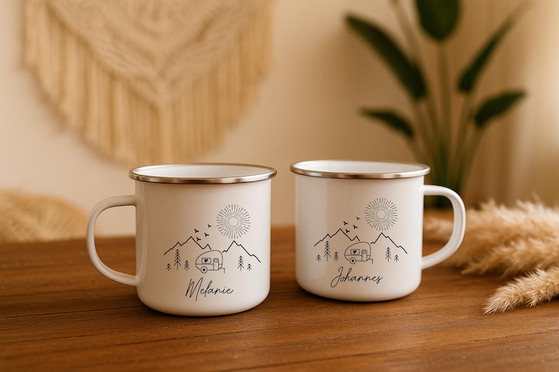 May include: Two white enamel mugs with silver rims, each featuring a black mountain and camper design. One mug has the name "Melanie", the other "Johannes". The design includes a sun, birds, and trees.