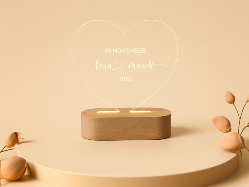 May include: A heart-shaped LED light with the text "20 NOVEMBER, Lara & Marek, 2025" displayed on a wooden base. The light emits a warm glow, ideal for a wedding or anniversary gift. The background is a soft beige.
