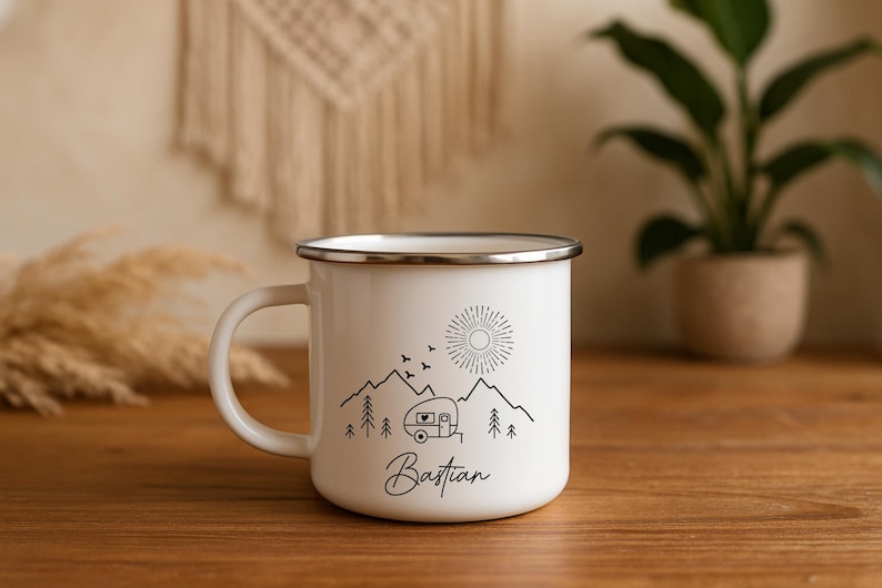 May include: White enamel camping mug with a black mountain and camper design. The mug features a sun, birds, and trees, with the name "Bastian" in script. The mug has a silver rim and handle.