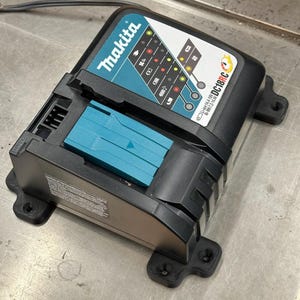 Könnte beinhalten: Ein schwarzes und türkises Makita DC18RC Batterieladegerät mit Statusanzeigefeld. Das Gerät verfügt über einen türkisen Akkuschacht, ein Netzkabel und aufgedruckten Text zur Kompatibilität mit 14,4V-18V Li-Ionen und 7,2V-14,4V Ni-MH Akkupacks.