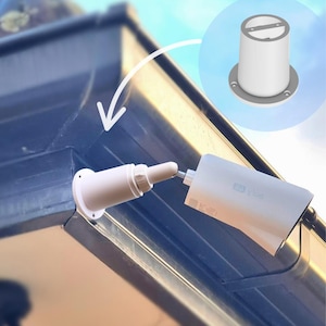 May include: White security camera system mounted on a dark blue surface. The system includes a camera, a mounting bracket, and a separate cylindrical component. The camera is connected to the bracket with a metal rod.