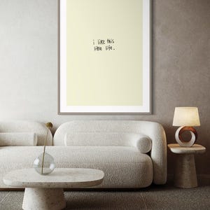 May include: A framed print with the text "i like this little life" in a minimalist style. The print is displayed above a white sofa and a speckled coffee table. A lamp and a glass vase with a dried flower are also visible.